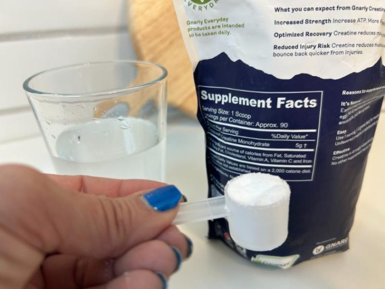 Woman holds a scoop of Gnarly Nutrition Creatine