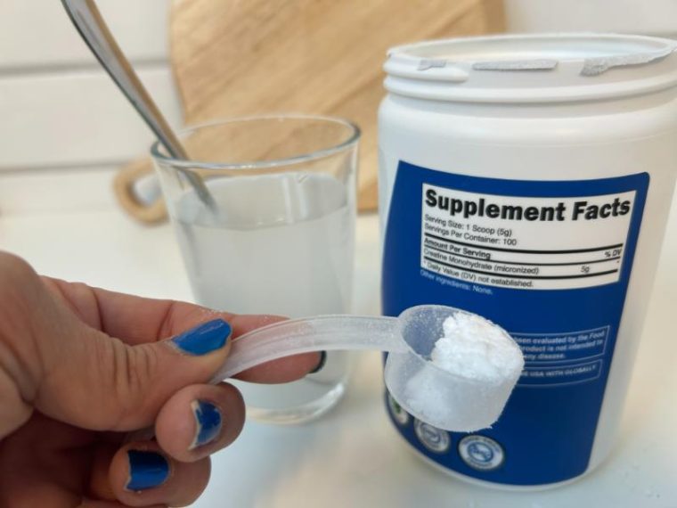 Woman holding a scoop of Nutricost Creatine with the supplement facts label displayed