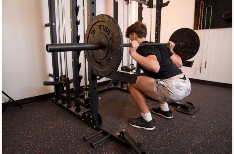 Young male athlete performs a barbell back squat.