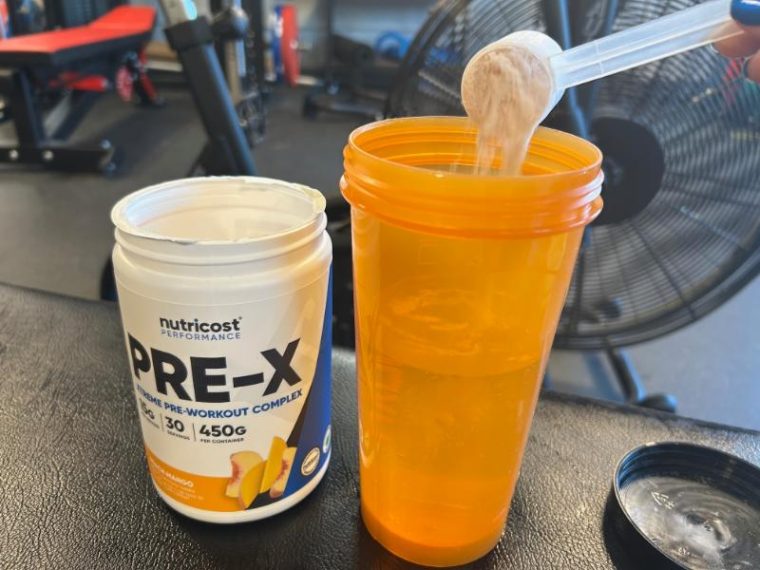 Pouring a scoop of Nutricost Pre-X into a shaker bottle.